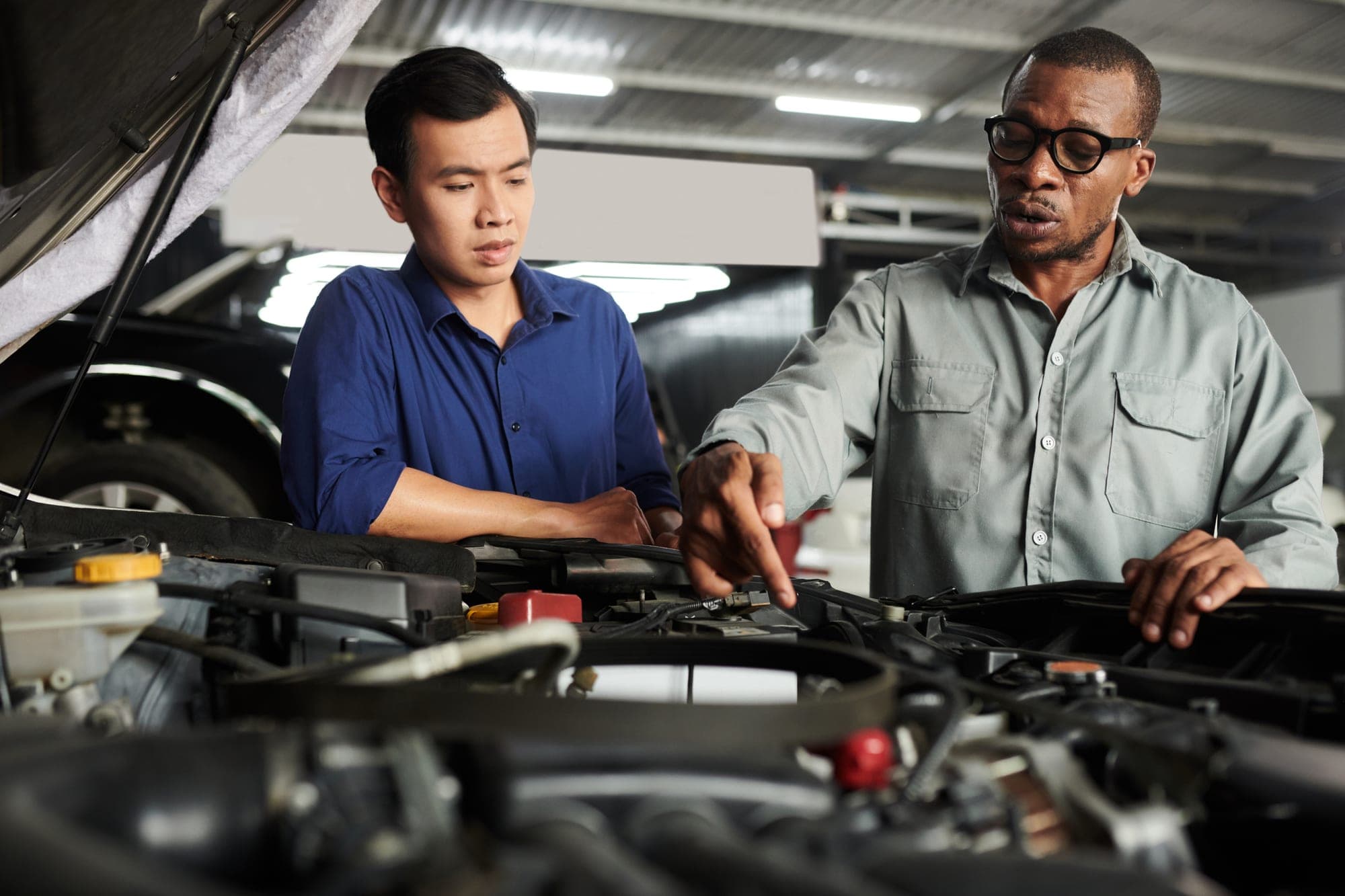 A mechanic pointing out a component under the hood to a customer in a repair shop